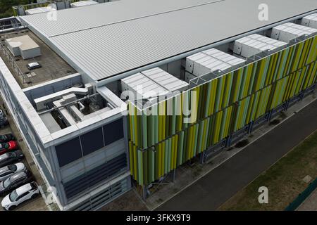 Luftbild eines modernen Rechenzentrumsgebäudes mit Klimaanlagen auf dem Dach, markanten grünen und gelben vertikalen Lüftungsschlitzen an der Fassade und einem angrenzenden Stockfoto