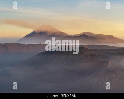Neblige vulkanische Grate und geschichtete Gipfel umgeben den Bromo unter einem leuchtenden Sonnenuntergangshimmel in Indonesien. Stockfoto