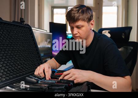 Junger Mann organisiert sorgfältig mehrere Speichermedien in einem speziellen Schutzkoffer, um sich auf ein Datenübertragungs- oder Videobearbeitungsprojekt vorzubereiten Stockfoto