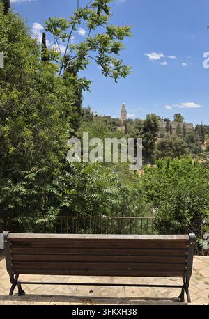 Holzbank in einem grünen Park mit einem malerischen Blick auf die Abtei der Entschlafung auf dem Zion in Jerusalem, Israel. Stockfoto