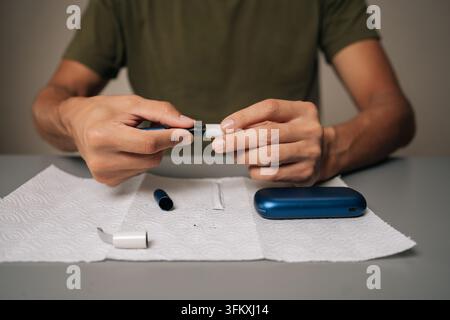 Zuschnitt eines nicht erkennbaren Mannes, der eine elektronische Zigarette mit einem Reinigungsstab und Papier auf dem Tisch reinigt, Wartung durchführt, um die ordnungsgemäße Funktion sicherzustellen Stockfoto