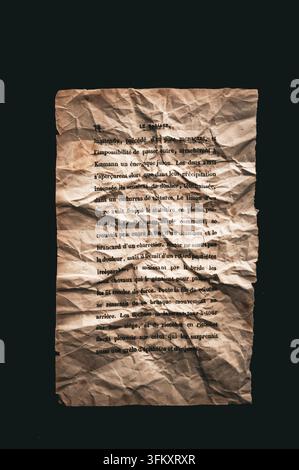 Zerknitterte antike französische Buchseite mit gealterter Typografie und zerrissenen Rändern, isoliert vor einem dunklen Hintergrund Stockfoto