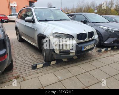 Ein silberner BMW X5 SUV, der auf einem äußeren, mit Ziegeln gepflasterten Parkplatz geparkt ist und erhebliche Schäden am vorderen rechten Kotflügel und der Stoßstange aufweist, die wurde Stockfoto