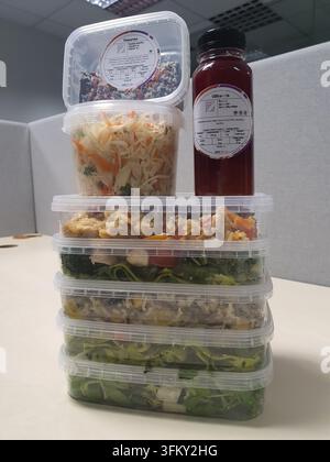 Eine Top-Down-Ansicht mehrerer Plastik-Mahlzeitvorbereitungsbehälter, die auf einer weißen Oberfläche angeordnet sind und verschiedene gesunde Lebensmittel enthalten, darunter Salate, Gemüse, Stockfoto