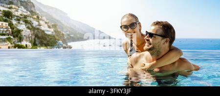 Paar hat zusammen Spaß in einem Infinity-Schwimmbecken mit Meerblick und der Stadt Positano im Hintergrund. Romantischer Italien-Sommerurlaub. Flitterwochen-Reise. Stockfoto