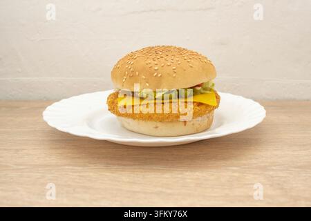Knuspriges paniertes Hühnersandwich mit Käse auf einem Sesambrötchen, serviert auf einem weißen Teller Stockfoto