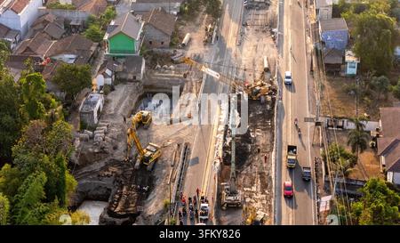 Indonesien - 24. September 2026: Luftaufnahme einer Straßenbaustelle mit Bagger, Kränen und Arbeitern auf einer belebten Straße mit Verkehr, umgeben von r Stockfoto