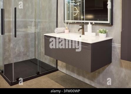 Stilvolles Badezimmerinterieur in grauen Betonfliesen, Dusche mit Glastür und modernem Waschbecken Stockfoto