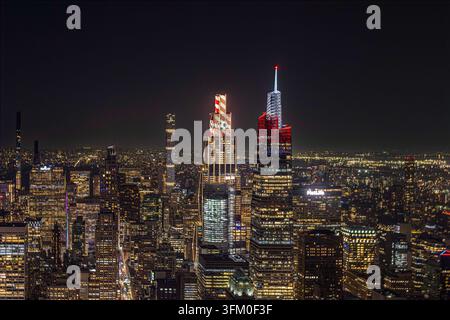 Eine nächtliche Stadtsilhouette von New York City zeigt markante Wolkenkratzer, die sich gegen den dunklen Himmel abzeichnen. Ein Gebäude zeigt einen Fußball. Stockfoto