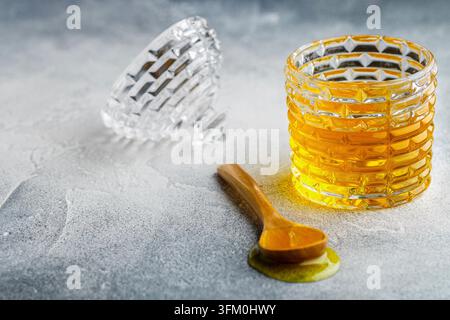 Flüssiger Blumenhonig in einem Glas mit hölzernem Honig-Dackel auf einem Beton- oder Stein-Hintergrund. Selektive Fokussierung, Kopierraum Stockfoto