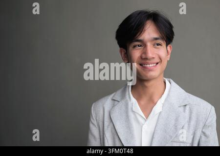 Horizontales Medium Close-up Porträt eines jungen nicht binären Geschlechterfluiden Thai Isan Geschäftsmann, der einen eleganten lässigen grauen Blazer und weißen Kragen trägt Stockfoto