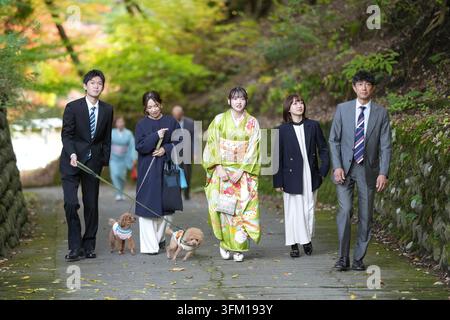 Eine Gruppe von Menschen geht einen Weg mit einem Hund an der Leine entlang. Die Menschen tragen traditionelle japanische Kleidung Stockfoto