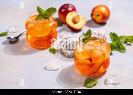 Nektarinen-Eistee-Getränke mit frischer Minze, Eiswürfeln und geschnittenen Pfirsichen ergeben ein lebendiges, erfrischendes Sommergetränk auf einem hellgrauen Hintergrund Stockfoto