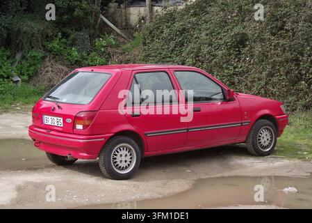 Roter Ford Fiesta MK3, der auf einem Feldweg in der Nähe eines Teiches und grüner Büsche geparkt ist Stockfoto