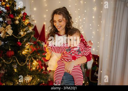 Mutter hält Baby in der Hand und feiert Weihnachten zu Hause Stockfoto