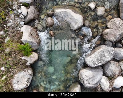 Klares Wasser fließt sanft durch glatte Steine. Die Wellen funkeln, während Wasser über runde Kieselsteine kaskadiert. Grünes Moos wächst am felsigen Rand. Dies ist Stockfoto