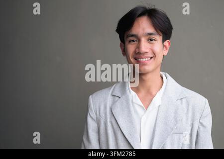 Horizontales Medium Close-up Porträt eines jungen, nicht binären Geschlechts fließenden Thai Isan Geschäftsmann, der einen eleganten lässigen grauen Blazer und ein weißes Hemd trägt. Das ist er Stockfoto