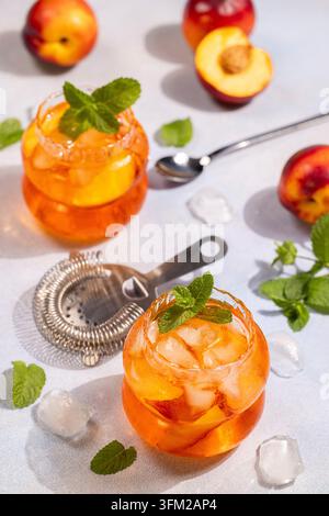 Zwei Gläser pfirsichgeschmackhafter Eistee mit Eiswürfeln und Pfirsichscheiben, garniert mit frischer Minze. Mit einem kühlen Sommergetränkerlebnis neben Loos Stockfoto
