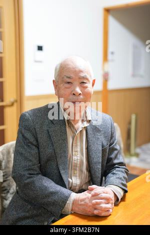 Ein älterer Mann sitzt an einem Tisch mit gefesselten Händen vor ihm. Er trägt einen grauen Anzug und ein weißes Hemd. Konzept der Ruhe und Fortsetzung Stockfoto
