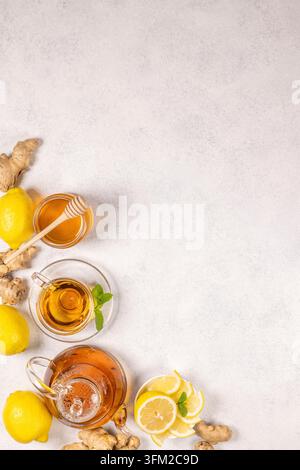 Heißer Ingwer-Zitronentee in einem Glas der Teekanne und serviert in einer Tasse neben frischen Zitronen, geschnittenem Ingwer, einer Schale mit Honig und einem Löffel sowie Minzblättern Stockfoto