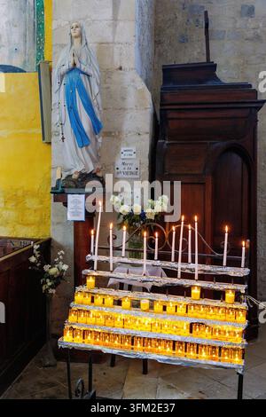 Beleuchtete Votiv- und Gebetskandeln mit einer Statue der seligen Jungfrau Maria in der Kirche Saint-Martin (St. Martinskirche) in Veules-les-Roses am Stockfoto