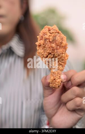 Nahaufnahme einer Geschäftsfrau, die draußen knuspriges gebratenes Hühnerstück hält. Vertikale Nahaufnahme mit Fokus auf einem goldenen, frittierten Geflügeltrommeln Stockfoto