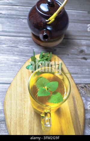 Frisch gebrühter Kräuter-Minz- und Zitronenmelissen-Tee in einer Glas Tasse mit keramischer Teekanne auf rustikaler Holzplatte, Top-Down-Blick, entspannendes Wellness-Ritual Stockfoto