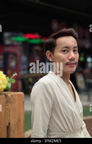 Ein professionelles Premium-Porträt eines selbstbewussten thailändischen, nicht-binären schwulen Mannes, der mit einem sanften Lächeln direkt in die Kamera blickt. Die einzelnen Funktionen sh Stockfoto