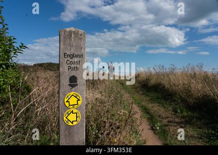 Eine Frau und ein Kind wandern den England Coast Path in Kent und folgen einem hölzernen Wegweiser, um den malerischen nationalen Küstenpfad zu erkunden. Stockfoto