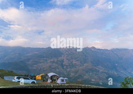 Campingplatz mit Zelten und Autos auf einem Bergrücken mit Blick auf eine schroffe Bergkette unter rosa Abendwolken, Ta Xua, Son La, Vietnam Stockfoto