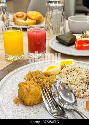 Ein traditionelles indonesisches Frühstücksbuffet mit gebratenem Reis, Nudeln und Eiern, serviert mit Gläsern frischem Orangen- und Guaven-Saft in einem Restaurant Stockfoto