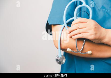 Gesundheitsfachkraft in blauer OP-Kleidung hält ein Stethoskop am Arm, repräsentierend klinische Praxis, medizinische Bereitschaft, Pflege und Hea Stockfoto