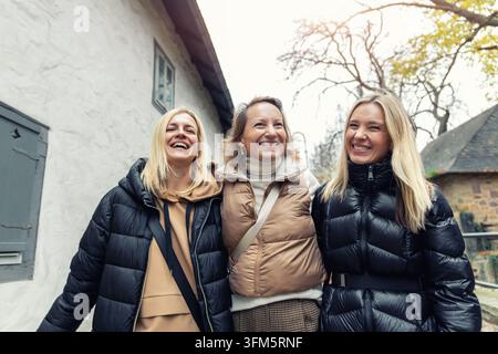 Fröhliche Freunde lachen gemeinsam bei einem herbstlichen Stadtbummel, teilen Umarmungen und freudige ReiseMomente. Ein authentisches Gruppenporträt fängt Freundschaft und Wiedersehen ein Stockfoto