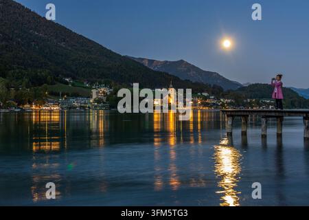 St. Wolfgang im Salzkammergut: Wolfgangsee, Stadt und Kirche St. Wolfgang, Vollmond, Frau auf Bootssteg, die in Salzka Fotos macht Stockfoto