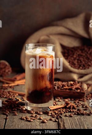 Eiskaffee mit Sahne. Auf einem alten Holztisch liegt eine Tüte gerösteter Kaffeebohnen und über den Tisch verteilt sind Zimtstangen, Muskatnuss und ein Stockfoto