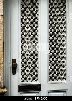 Vintage weiße Holztür mit kunstvollen Eisengitter-Fenster Einsätzen. Nahaufnahme einer eleganten Vintage weißen Tür mit detailliertem Metallgitter-Gitterwerk Stockfoto