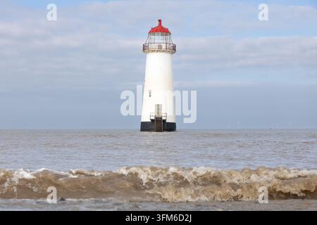 Eine Welle bricht im Vordergrund vor dem Point of Ayr Leuchtturm vor der walisischen Küste. Stockfoto