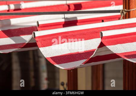 Nahaufnahme eines gelochten rot-weiß gestreiften Markisendachs vor einem Café in Tallinn, Estland, das im Sonnenlicht weiche Schatten wirft Stockfoto