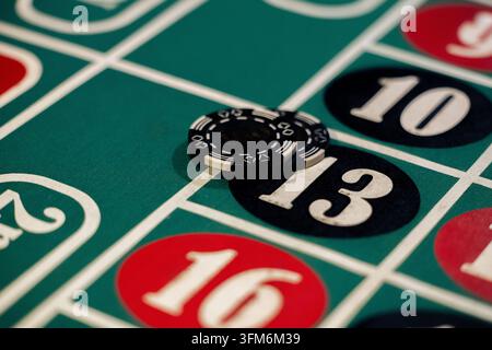 Casinoscheiben liegen auf der Glückszahl dreizehn auf grünem Roulettetisch. Gestapelte Jetons bedecken das Feld unter hellem Licht. Stockfoto