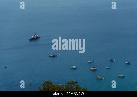 Luftbild eines großen, luxuriösen Yachts und mehrerer kleiner Segelboote, die in den ruhigen, dunkelblauen Gewässern des Mittelmeers in der Nähe von Taormina, Sizilien, Italien vor Anker liegen Stockfoto