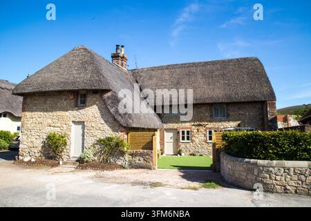 Außenansicht eines traditionellen, aus Stein gebauten englischen Landhauses mit Strohdach und kleinem grünen Rasen an einem klaren Sonnentag in Großbritannien. Stockfoto