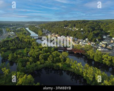 Brücken überspannen einen Fluss mit klarem Wasser, das den blauen Himmel und die Vegetation widerspiegelt. In der Nähe sind Gebäude und Freiflächen sichtbar. Die Szene wurde im Stockfoto