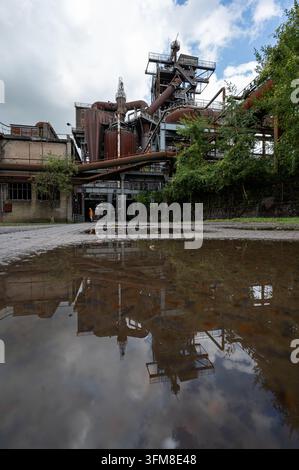 Hochofen und bewölkter Himmel spiegeln sich in einer großen Pfütze im Landschaftspark Duisburg-Nord, Deutschland Stockfoto