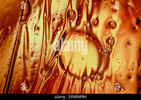 Abstrakte Textur, die sich mit goldenen Öltropfen und Luftblasen bildet, die sich in einer zähflüssigen Flüssigkeit vermischen und die Fluiddynamik zeigen Stockfoto