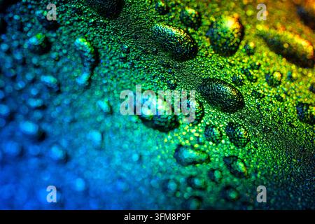 Nahaufnahme von Wassertropfen, die an einer strukturierten Kunststoffoberfläche haften und einen lebendigen Grün-, Blau- und Gelbgradient reflektieren Stockfoto
