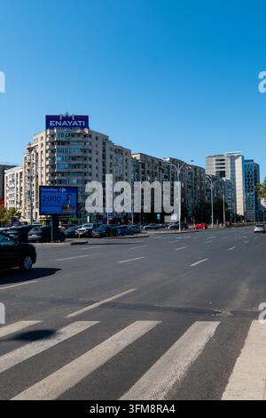 Straßensicht der Piata Victoriei in Bukarest mit Wohnblocks, einem Fußgängerüberweg, geparkten Autos und Werbetafeln auf den Dächern. Stockfoto