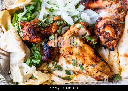 Gegrillte Hühnerflügel im Nahaufnahme mit frisch geschnittenen Zwiebeln und grünen Kräutern, serviert auf Lavash-Brot in einer Aluminiumfolien-Schale Stockfoto