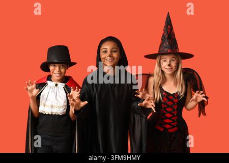 Halloween-Feier und Kinderspaß, diverse Gruppe von Kindern in gruseligen Kostümen, die mit verspielten Ausdrücken vor einem orangefarbenen Studiohintergrund posieren Stockfoto