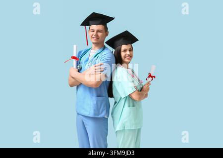 Medizinische Ausbildung und Karrierenerfolg, junge Ärzte in Doktorhüten, die mit Stolz und beruflichem Erfolg Diplomata auf blauem Hintergrund halten Stockfoto