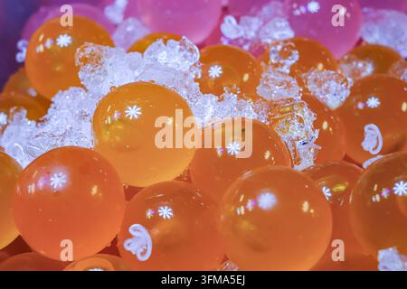 Gekühlte durchscheinende orangefarbene Geleekugeln, die auf zerkleinertem Eis an einem Süßwarenstand auf einem Straßenmarkt im Freien ruhen, Nahaufnahme. Stockfoto